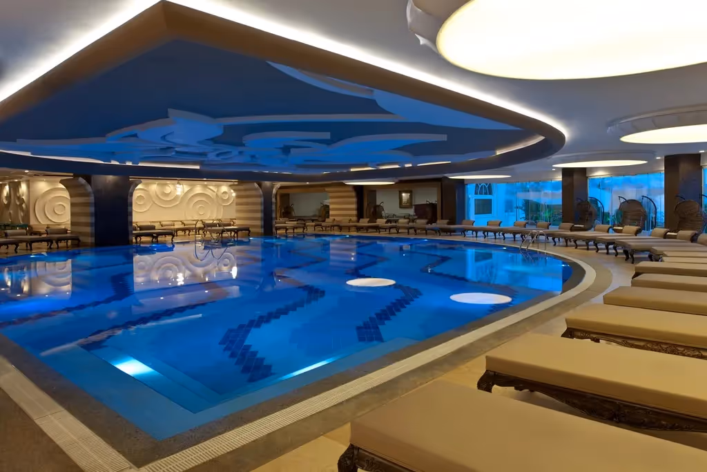 Het binnenzwembad van Delphin Imperial met verlicht plafond en ligbedden langs de rand