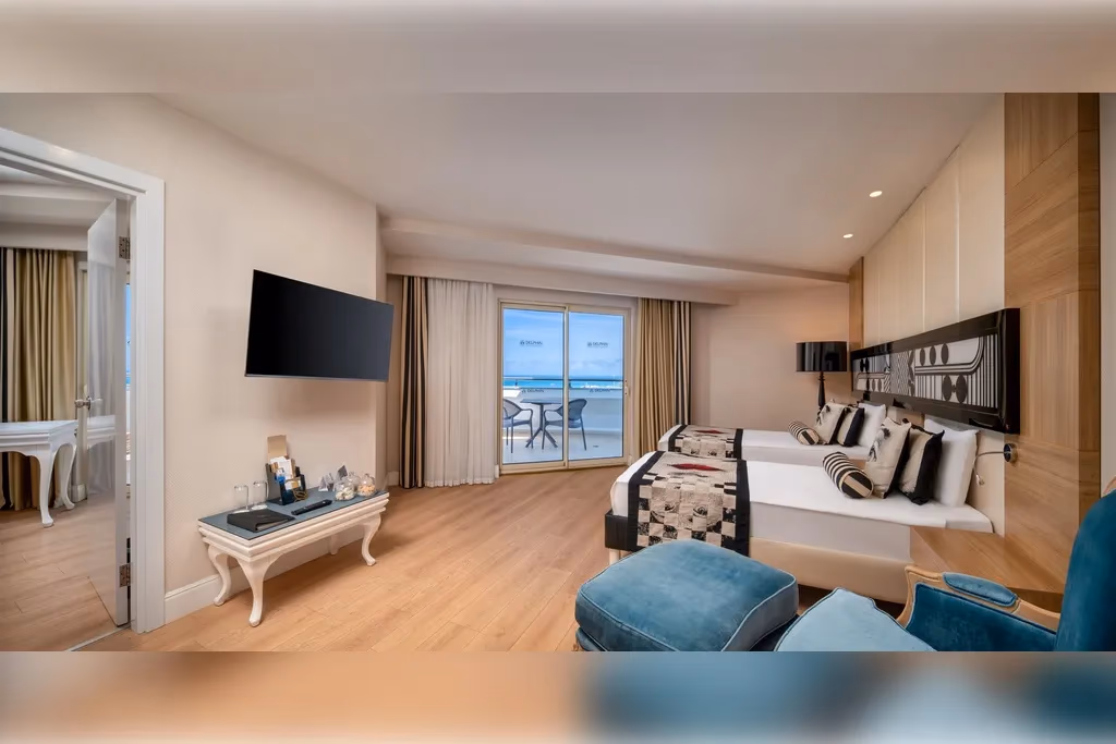 Deluxe familiekamer van Delphin Imperial in Lara met zithoek, tweepersoonsbed en een deur naar het terras met zeezicht