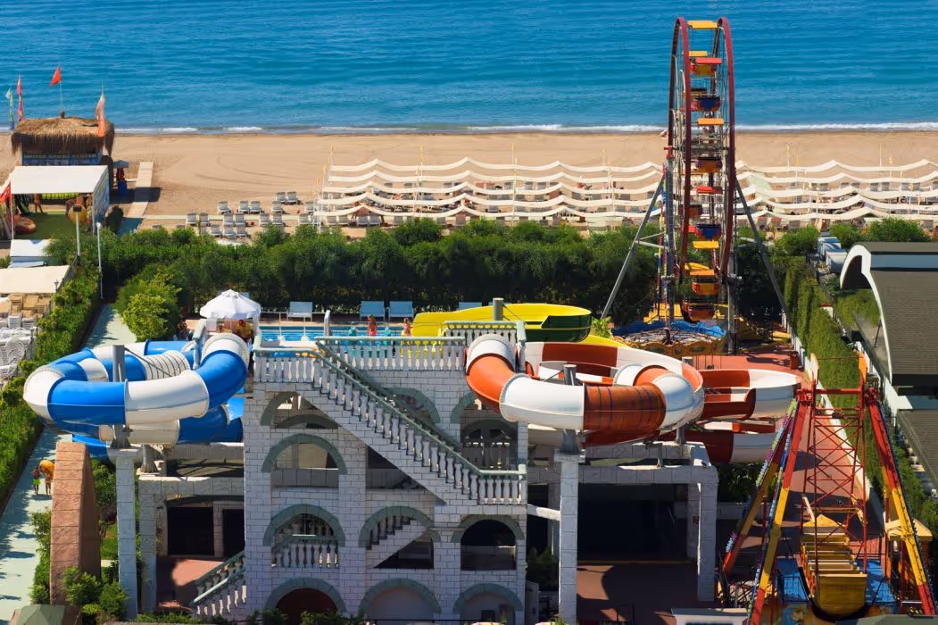 Glijbanen boven een wit gebouw met trappen, met een reuzenrad, het strand en de zee op de achtergrond bij Delphin Imperial in Lara