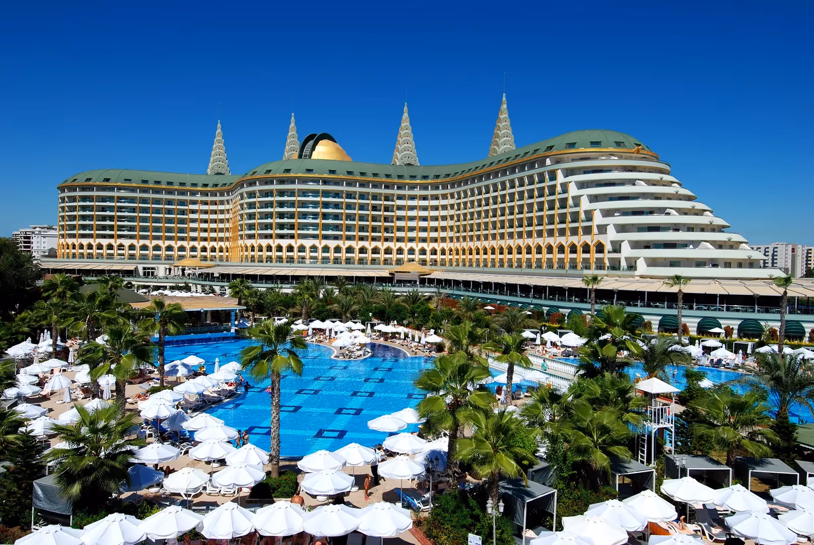 Het hoofdgebouw van Delphin Imperial in Lara met het grote zwembad, palmbomen en witte parasols op de voorgrond