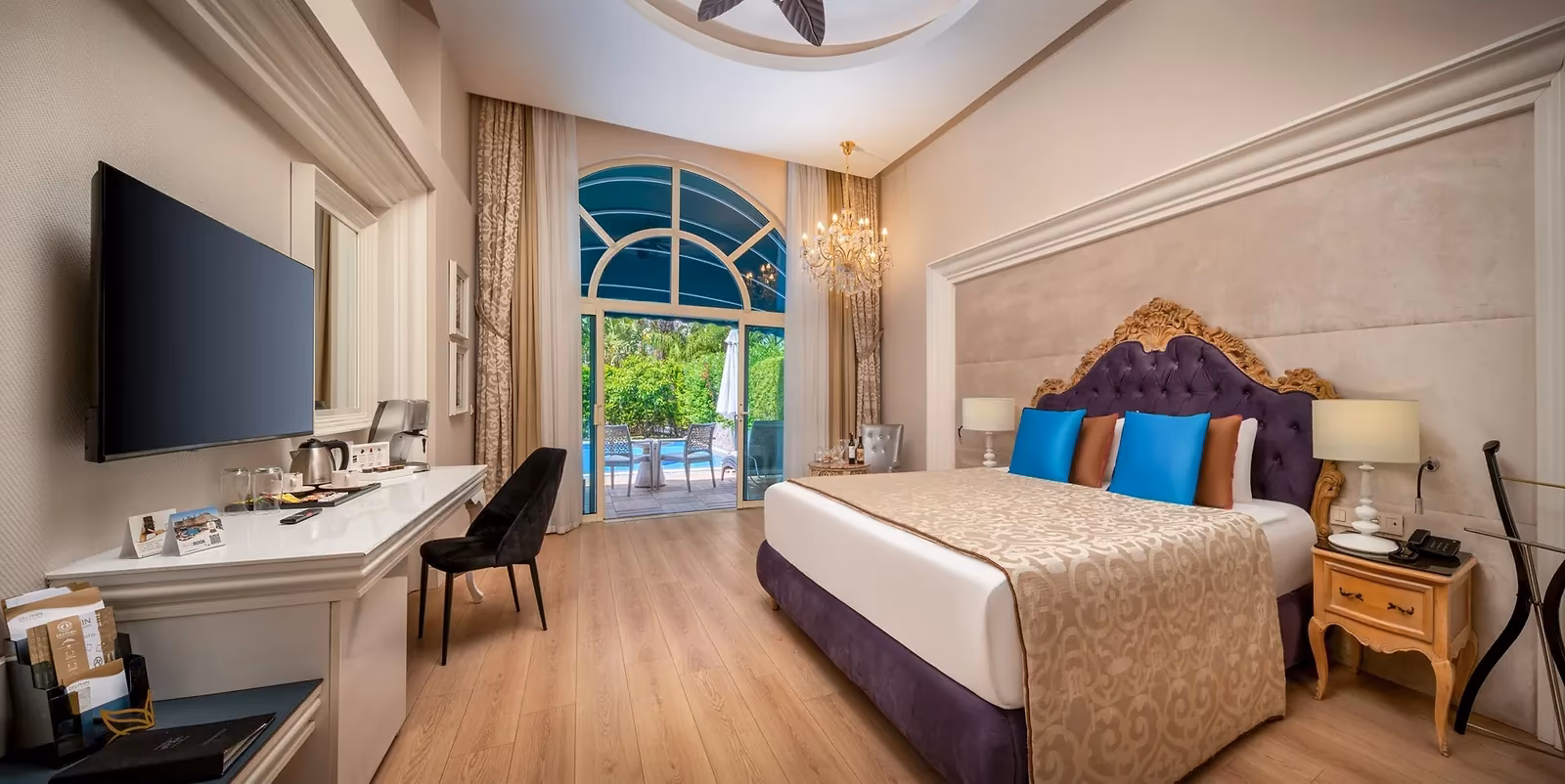 Kamer met tweepersoonsbed, bureau en een boogdeur naar een terras aan het zwembad in Delphin Imperial in Lara