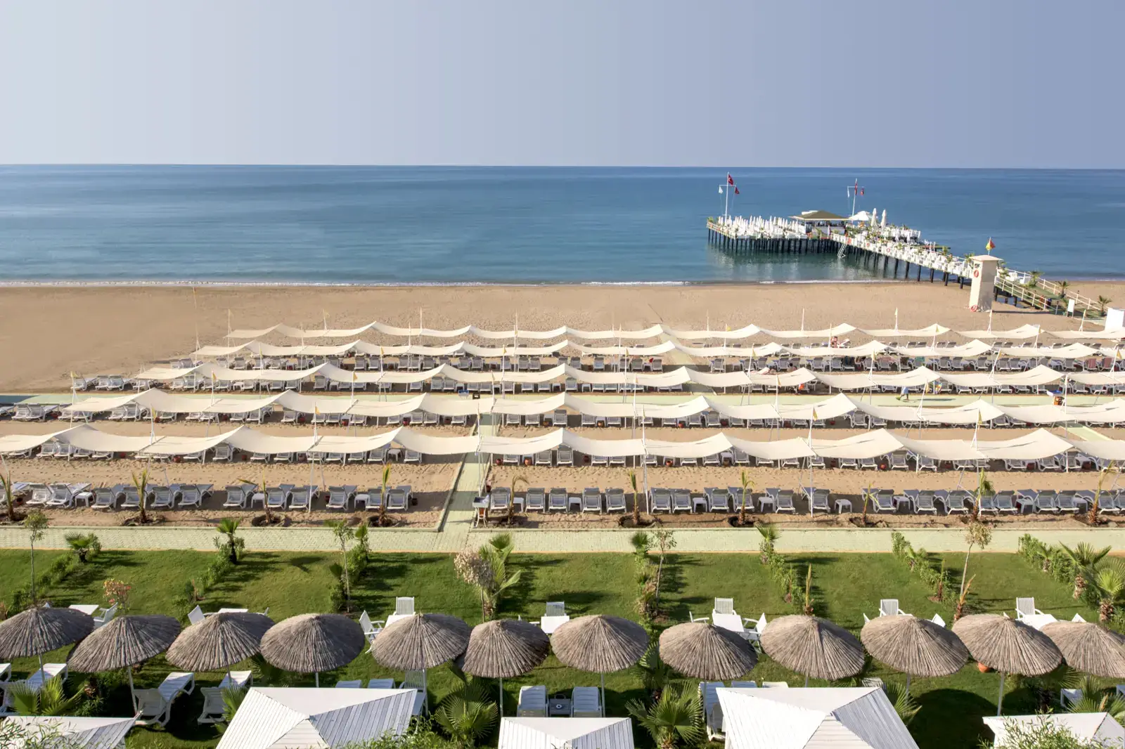 Het strand van Delphin Imperial met rijen ligbedden, parasols en de steiger in zee