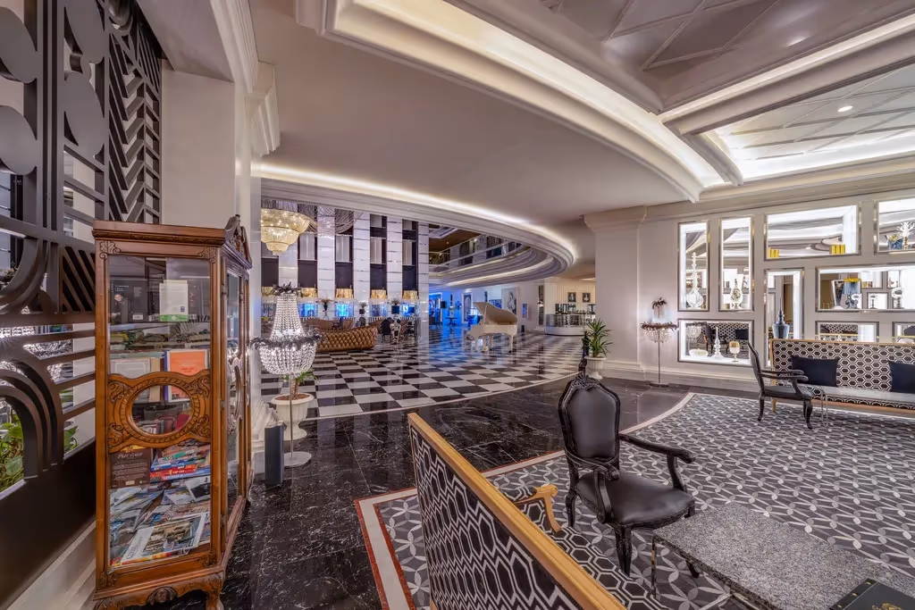 Zithoek in de lobby van Delphin Imperial in Lara met zwarte stoelen op een zwart-wit tapijt, met daarachter een witte vleugel en kroonluchters