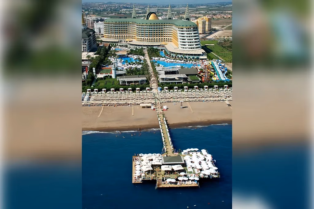 Luchtfoto van Delphin Imperial in Lara met de lange steiger in zee, het strand, de zwembaden en het gebogen hoofdgebouw