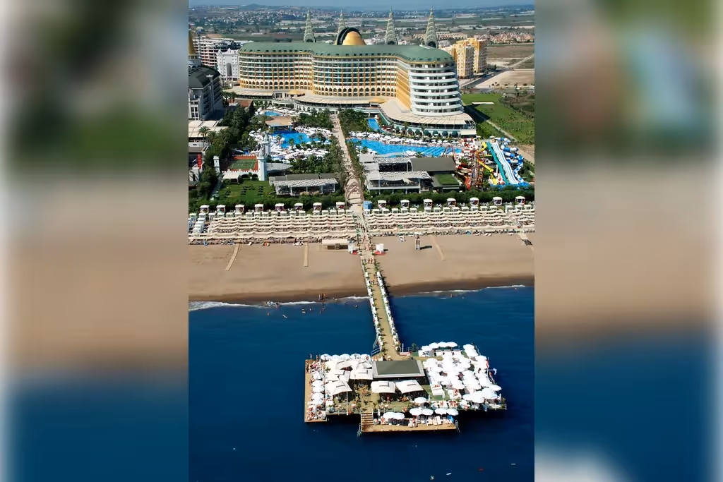 Luchtfoto van Delphin Imperial in Lara met de lange steiger in zee, het strand, de zwembaden en het gebogen hoofdgebouw
