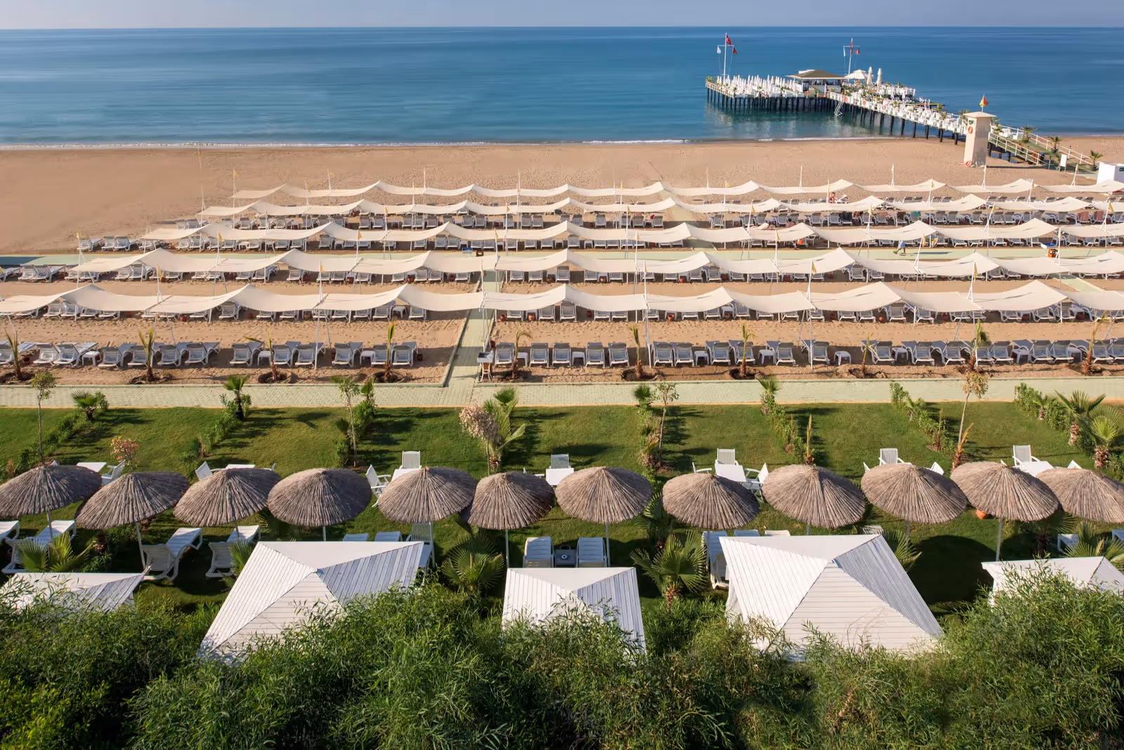 Strand van Delphin Imperial met rijen witte parasols, strandhuisjes met rieten daken en de steiger in zee