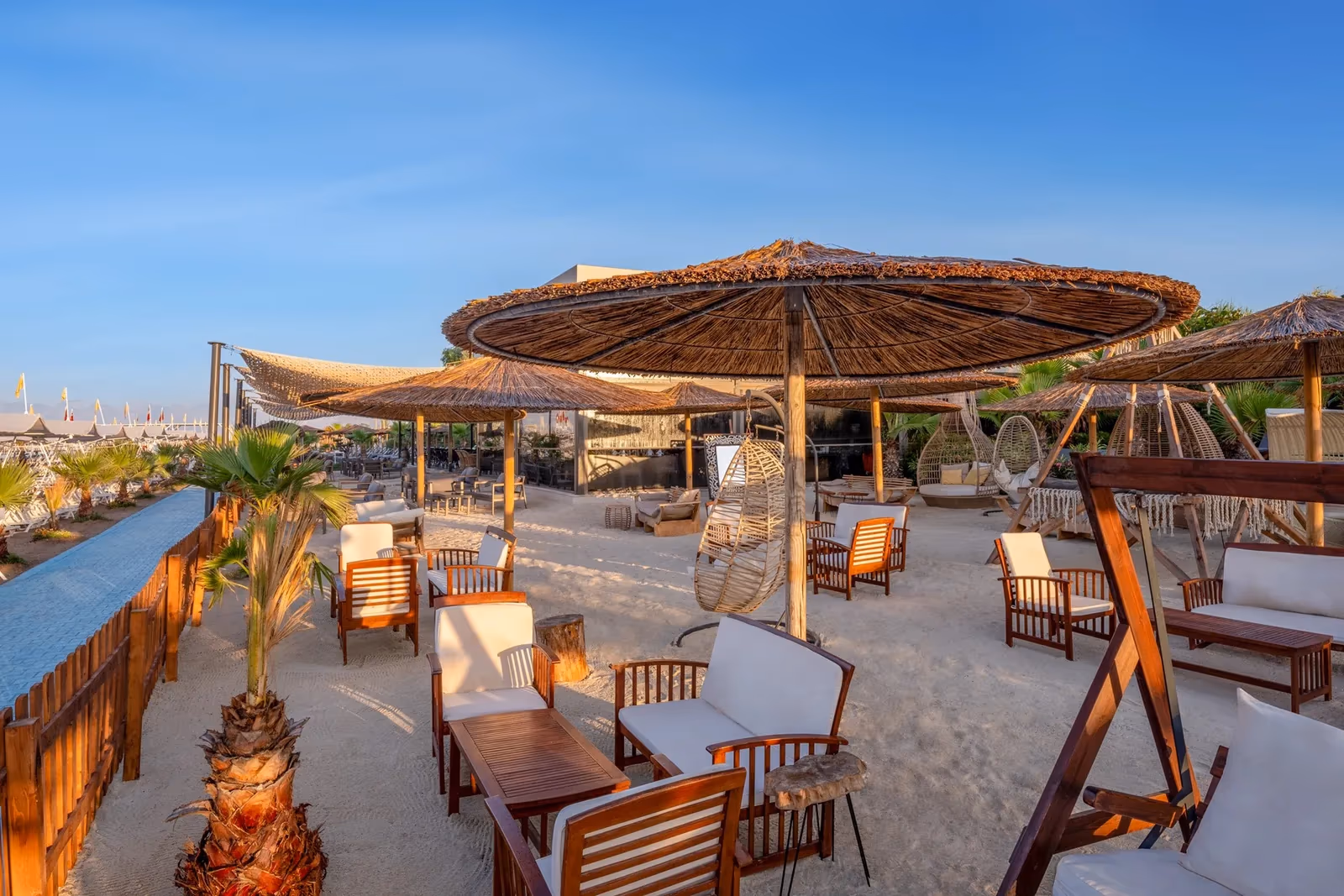 Loungeplek op het zand met rieten parasols, banken en hangstoelen bij Delphin Imperial in Lara