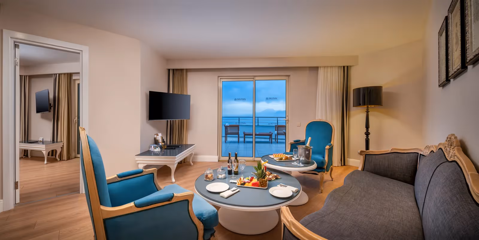 Woonkamer van de suite in Delphin Imperial met zitbank, fauteuils, eettafel en een terras aan zee