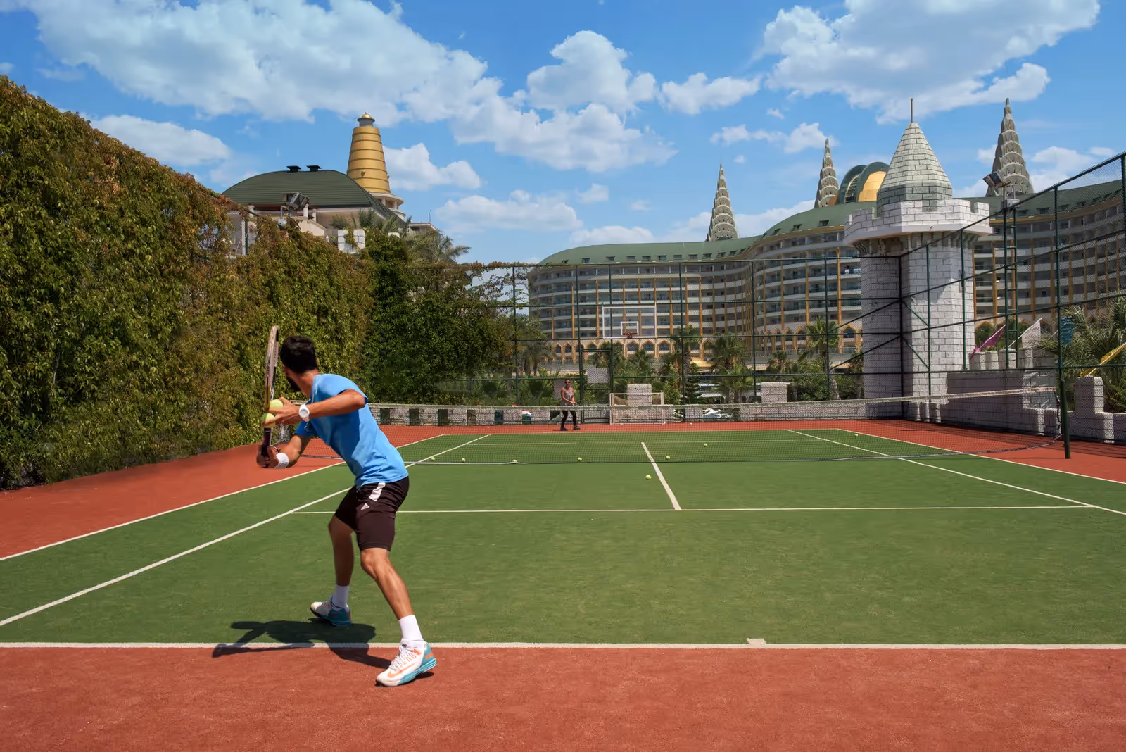Tennisbaan van Delphin Imperial met een tennisser, met het hoofdgebouw op de achtergrond