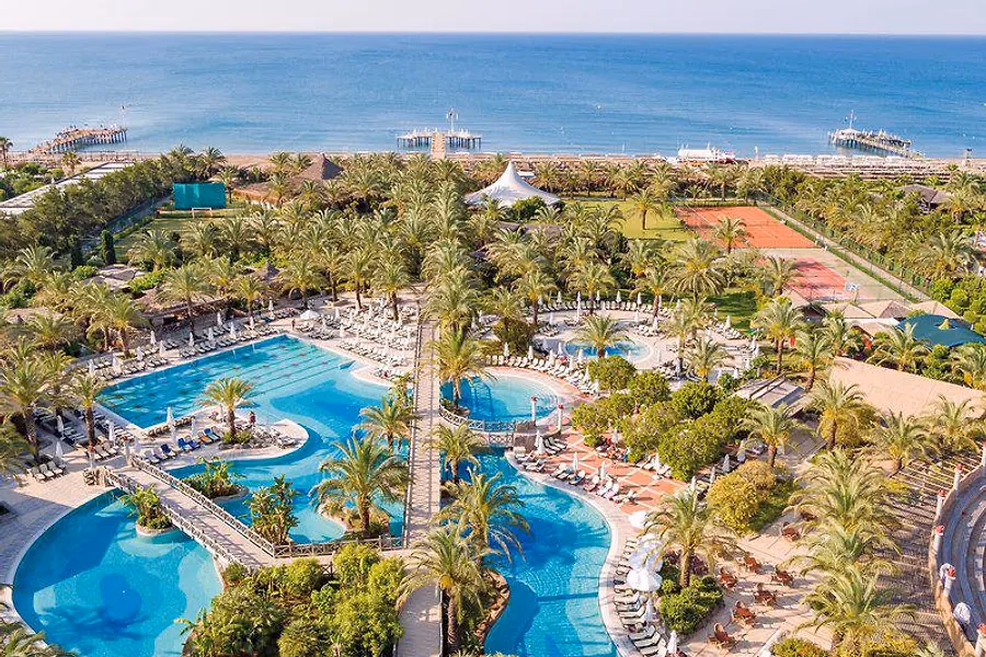 Luchtfoto van de zwembaden tussen de palmbomen van Hotel Royal Wings in Lara, met de zee erachter